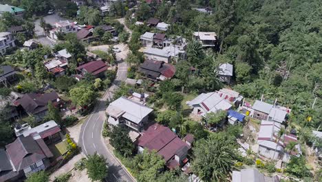 Indian-village-with-road-snaking-through,-surrounded-by-lush-vegetation-of-tropical-forest,-drone-footage