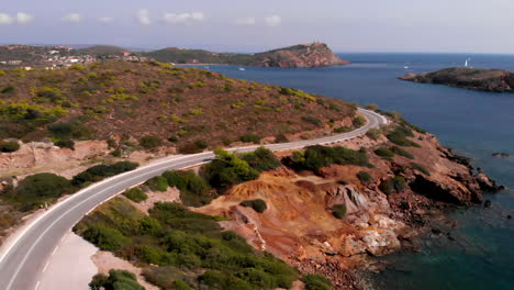 Car-disappears-behind-corner-on-winding-road-at-Cape-Sounion,-static-aerial