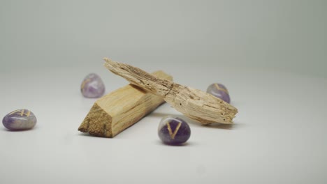 Two-Pieces-Of-Palo-Santo-Wood-Surrounded-By-Purple-Gem-Stones-Moving-In-A-Circular-Motion---Close-Up-Shot