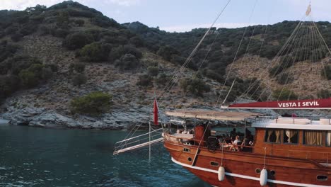 Aerial,-low-flying-shot-of-a-stunning-wooden-boat-in-a-bay-of-the-Mediterranean-Sea,-liveaboard