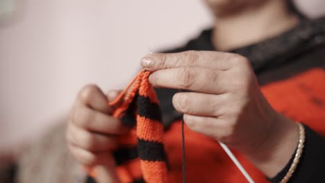 Close-up-from-below-of-woman's-hands-knitting-a-scarf-in-red-and-black-color