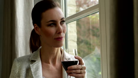 Adult-woman-stands-besides-window-drinking-glass-of-red-wine-close-up