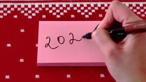 Writing-year-twenty-twenty-on-pink-Post-It-note-against-red-design-background