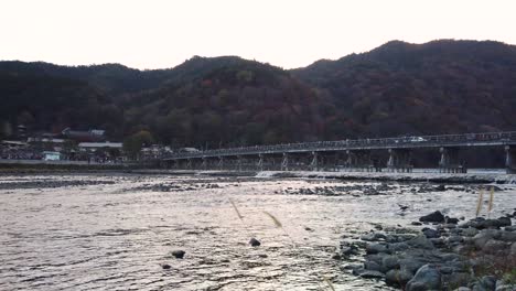 Togetsukyo-bridge,-slow-motion-pan-as-sun-sets-over-Arashiyama-in-Kyoto,-Japan