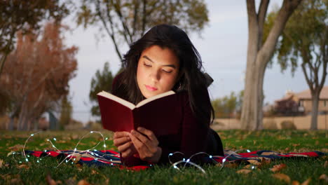 A-young-adult-woman-reading-a-book-and-using-her-imagination-to-bring-the-story-to-life-outdoors-in-the-park-at-sunset