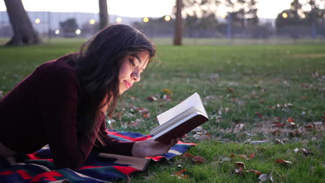 Eine-Junge-Hispanische-Frau,-Die-Ein-Buch-Liest-Und-Sich-Bei-Sonnenuntergang-Im-Park-Entspannt
