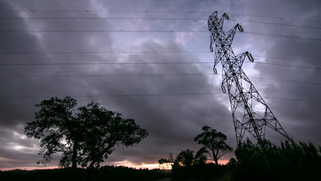 Dramatische-Wolken-über-Silhouettierten-Elektrischen-Leitungen-Und-Pylonen,-Zeitraffer