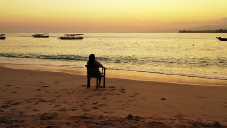 Einsames-Mädchen,-Das-Schöne-Dämmerungsfarben-Mit-Gelbem-Himmel-Beobachtet,-Der-über-Ruhige-Lagune-Reflektiert,-Die-Sand-Des-Exotischen-Strandes-In-Bali-Wäscht