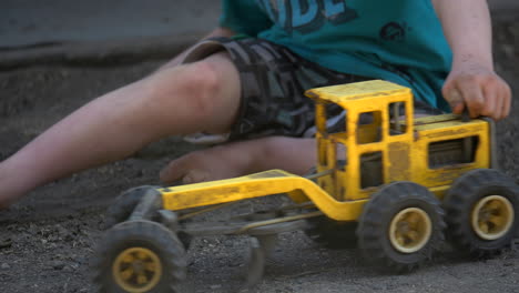 Young-Boy-Playing-With-A-Toy-Grader-Truck-In-The-Dirt