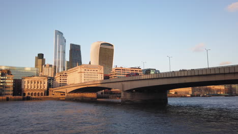 Red-British-bus-driving-downtown-over-a-bridge-towards-skyline-of-skyscrapers