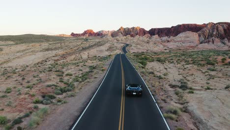 Black-Ferrari-sports-car-driving-into-frame-on-a-desert-highway-in-the-Valley-of-Fire,-Nevada,-USA,-at-sunset