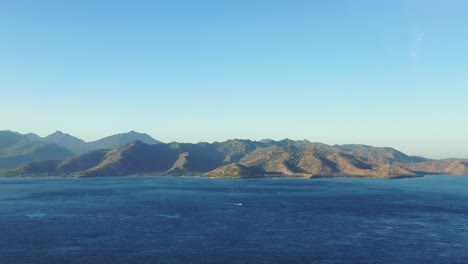 Volcanic-mountains-of-Lombok,-Indonesian-islands-under-warm-light-of-sunset,-surrounded-by-deep-blue-sea-on-a-bright-sky-background