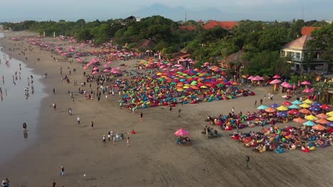 Fly-over-of-famous-double-six-beach-crowded-by-tourists,-aerial,-Bali
