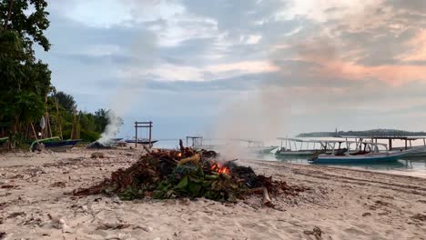 Tilt-down-shot-of-burning-waste-and-leaces-on-exotic-beach-in-Gili-Air-Island