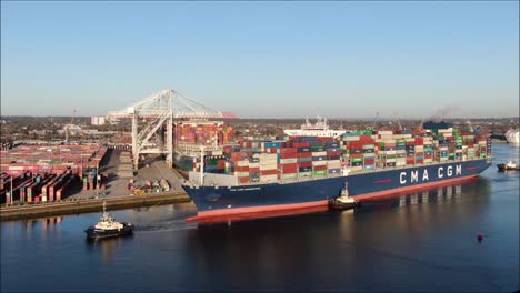 A-large-CMA-CGM-container-ship-arrives-into-southampton,-fast-zoom-shot-with-tugs-and-rising-drone