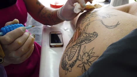 Close-of-tattoo-artist-painting-a-snake-on-white-client's-leg