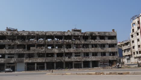 Steady-shot,-cars-passing-the-road,-old-huge-infrastructure-damaged-by-Syrian-civil-war-in-Homs-city
