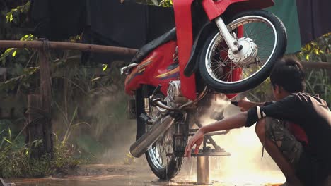 Close-Shot-of-a-Red-Moped-Being-Cleaned-with-a-Hose-by-an-Asian-Man