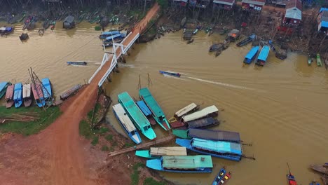 Two-Boat-Sailing-Over-The-Mekong-River-Under-The-Bridge-In-Kompong-Khleang-In-Cambodia-With-Boats-Docked-On-The-Riverside---Aerial-Shot