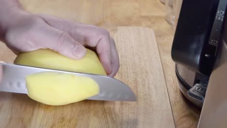 Slow-Motion-Slider-Shot-of-Slicing-a-Potato-on-a-Wooden-Chopping-Board-in-the-Kitchen