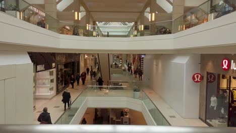 Blick-über-Ein-Geländer-Auf-Ebenen-In-Einem-Großen-Einkaufszentrum-Mit-Glas-Und-Chrom-Und-Käufern,-Die-Darin-Spazieren-Gehen