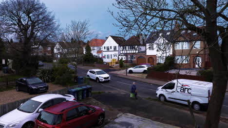 A-typical-street-in-Harrow,-London,-UK,-with-houses-and-cars-parked-and-a-female-walking-home-after-shopping.
