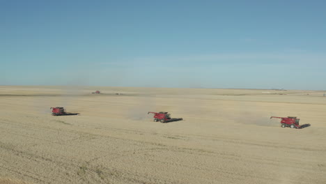 Group-of-three-combine-harvesters-cutting-a-good-standing-crop-of-golden-ripe-wheat--dolly-in-aerial-shot