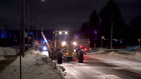 Snow-removal-vehicles-working-on-a-snowy-road-at-night-in-a-suburban-area