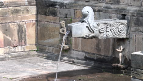 Water-pouring-out-of-a-stone-water-spout,-dhunge-dhara-or-hiti-at-a-Hindu-temple-at-the-UNESCO-World-Heritage-Site-of-Patan-Durbar-Marg-in-Kathmandu,-Nepal