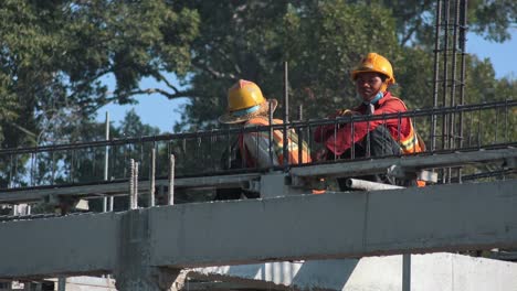 Wide-Shot-of-Two-Construction-Guys-on-the-Roof-Of-a-Building-On-a-Construction-Site-Having-Rest-in-the-Hot-Sun