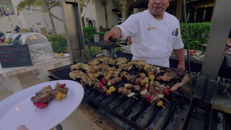 Adult-male-Mexican-Chef-places-shish-kabobs-onto-plate-of-Caucasian-person-at-an-outdoor-event