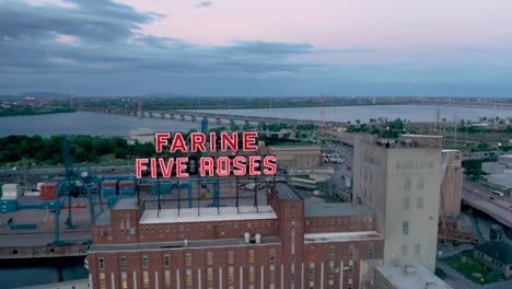 Drone-moving-up-in-front-of-the-iconic-Farine-Five-Roses-building-revealing-the-St-Lawrence-river