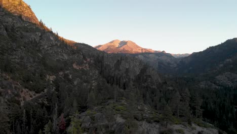 Aerial-pan-out-of-a-windy-road-through-Sonora-Pass-in-California-at-sunset-with-trees-in-the-foreground