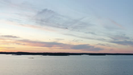 Aerial-view-of-birds-flying-with-a-colorful-dusk-sky-background,-on-the-coast-of-Porkkalaniemi,-in-the-archipelago,-sunny,-summer-evening-dusk,-in-Porkkala,-Gulf-of-Finland---tracking,-drone-shot