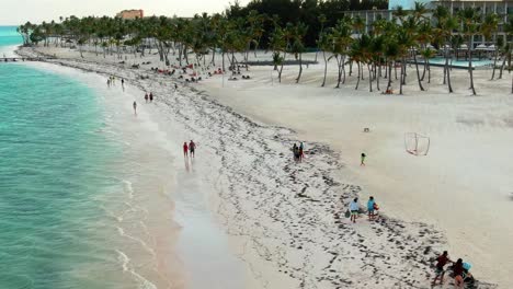Aerial,-sandy-white-beach-where-couples-walk-hand-and-hand-along-the-shore,-Dominican-Republic