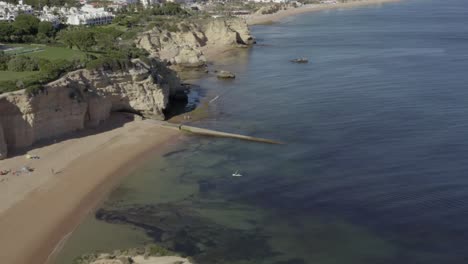 Flying-over-two-people-paddle-boarding-on-an-incredible-tropical-beach-surrounded-by-beautiful-oceanic-cliffs,-drone-aerial