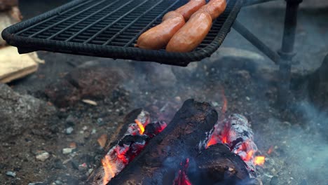 Sausages-getting-grilled-over-a-soldering-open-fire-flame-grill-outdoors,-with-copy-space