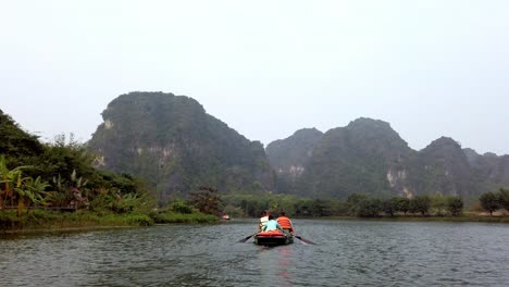 Tour-boat-with-tourists-and-guide-paddling-on-Day-River-overlooking-limestone-Kerst-mountain-landscape,-Handheld-shot