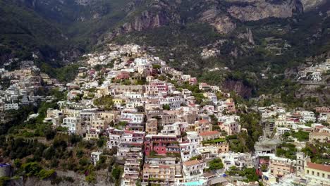 Positano-town-in-the-Italian-Amalfi-coastline-with-hillside-mansions-and-hotels-built-on-the-cliff,-Aerial-pedestal-lift-tilt-down-shot