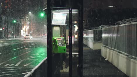 Phone-Booth-On-The-Sidewalk-Street-With-Cars-Travelling-At-Night-During-A-Heavy-Snow-In-Kyoto,-Japan