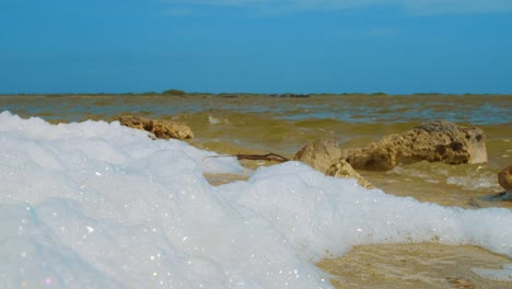 Salzwasserschaum-An-Land-Gespült-Mit-Meereswellen-Im-Hintergrund-In-Kralendijk,-Bonaire