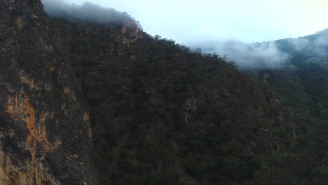 Aerial-drone-revealing-huge-rock-mountains-covered-in-thick-Australian-bush-land-on-a-foggy-winter-morning-in-the-Bungonia-National-Park-NSW-Australia