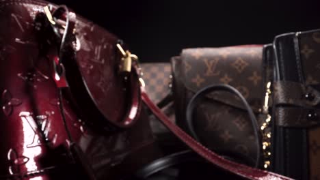 Macro-view-flying-past-luxury-leather-bags,-vintage-and-new-Louis-Vuitton-handbags-in-a-dark-scene-with-black-isolating-background,-expensive-products-for-the-rich