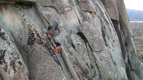 Three-climbers-ascending-by-a-granite-wall,-with-a-lake-in-the-back-ground