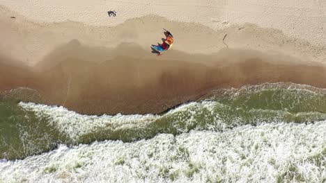AERIAL:-Top-View-Shot-of-Surfer-Coming-to-His-Wind-Kite-Placed-on-a-Sandy-Beach-in-Nida
