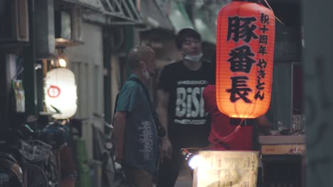 Japaner-Unterhalten-Sich-Mit-Abgenommenen-Masken-Unter-Dem-Hals-Vor-Einem-Restaurant-In-Kamata,-Tokio,-Japan