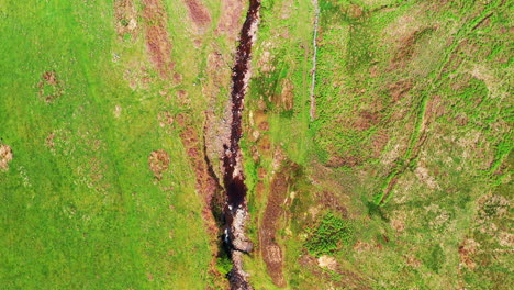 Aerial-top-down-shot-following-a-rocky-stream-in-the-middle-of-the-green-countryside,-sunny-bright-day
