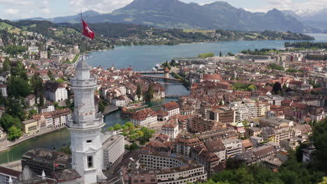 Drone-flying-past-Swiss-flag-on-castle-tower-and-revealing-the-beautiful-city-of-Luzern,-Switzerland