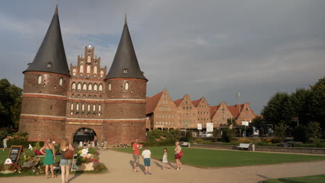 Pan-right-shot-of-famous-Holsten-Gate-building-with-visiting-tourists-during-sunset-in-evening-in-Lübeck,-Germany