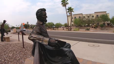 Medium-close-up-of-bronze-statue-of-Abraham-Lincoln-sitting-on-a-park-bench-looking-out-on-the-main-road,-Fountain-Hills,-Arizona